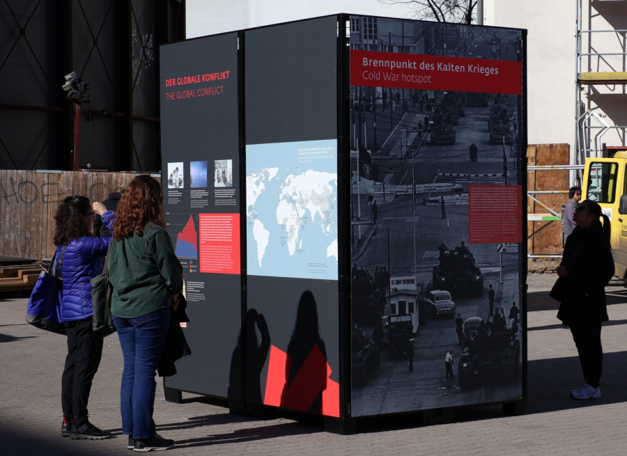 Drei Personen schauen sich eine große Ausstellungstafel an der Straße an