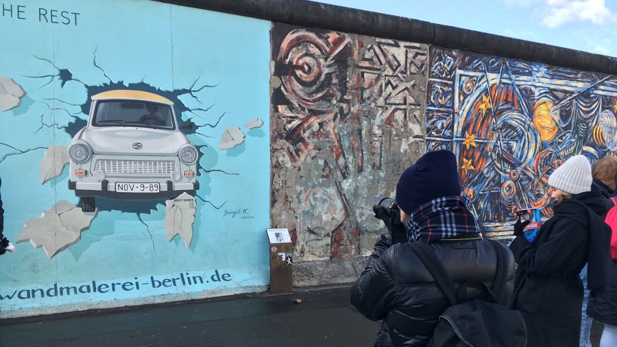 Ein Mensch steht fotografierend vor drei Bildern der East Side Gallery