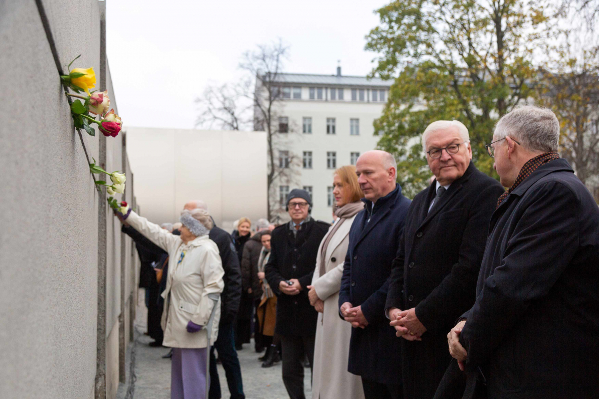 Die Gäste, darunter der Regierende Bürgermeister von Berlin Kai Wegner und der Bundespräsident Frank Walter-Steinmeier stecken bunte Rosen in die Hinterlandmauer