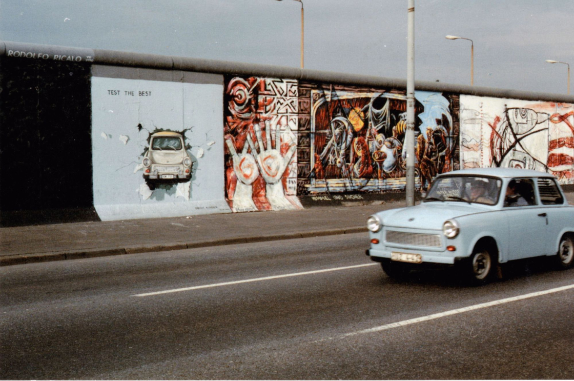 Trabi fährt an der East Side Gallery vorbei