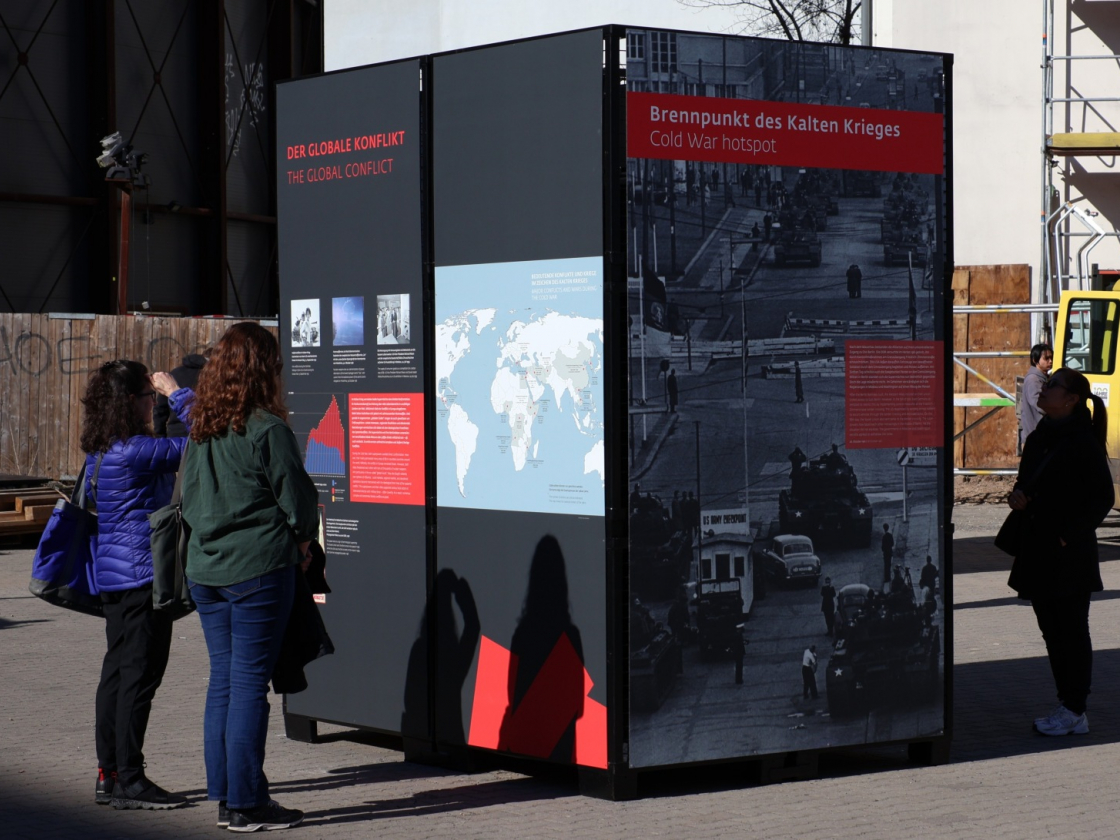 Drei Personen schauen sich eine große Ausstellungstafel an der Straße an