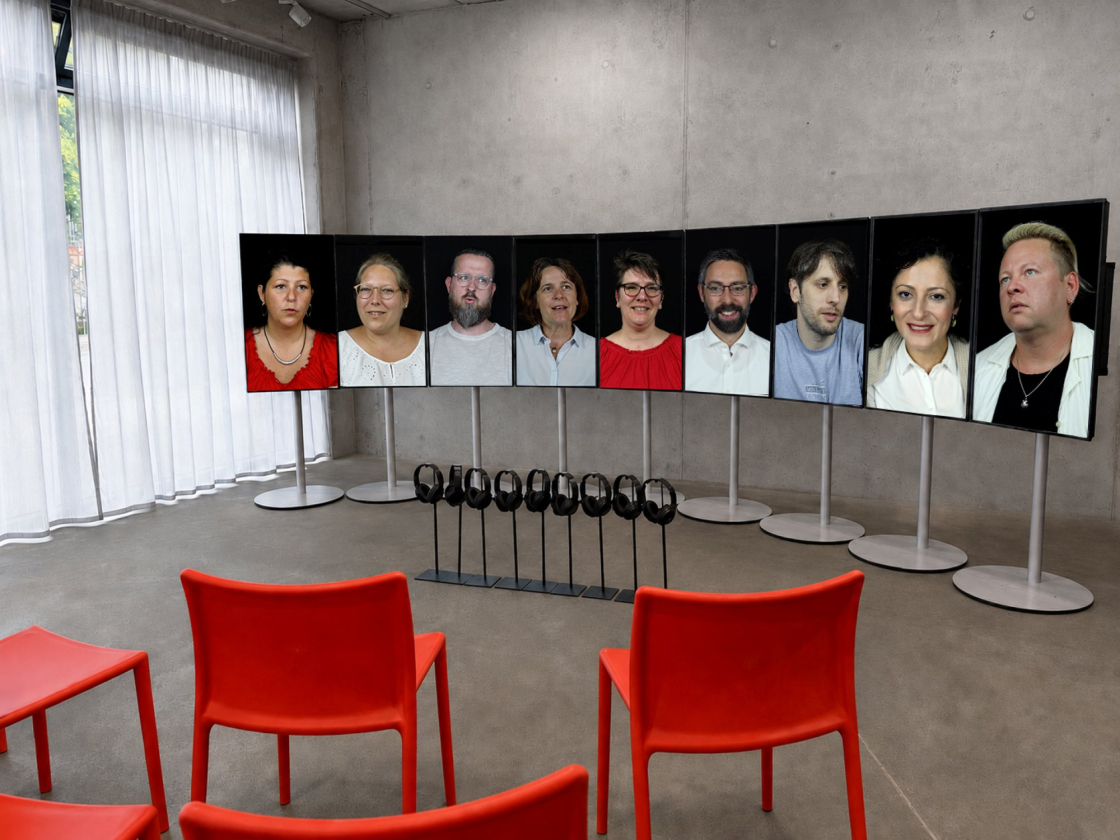 Neun Bildschirme mit den Gesichtern der Zeitzeuginnen und Zeitzeugen in einem Raum aufgebaut.