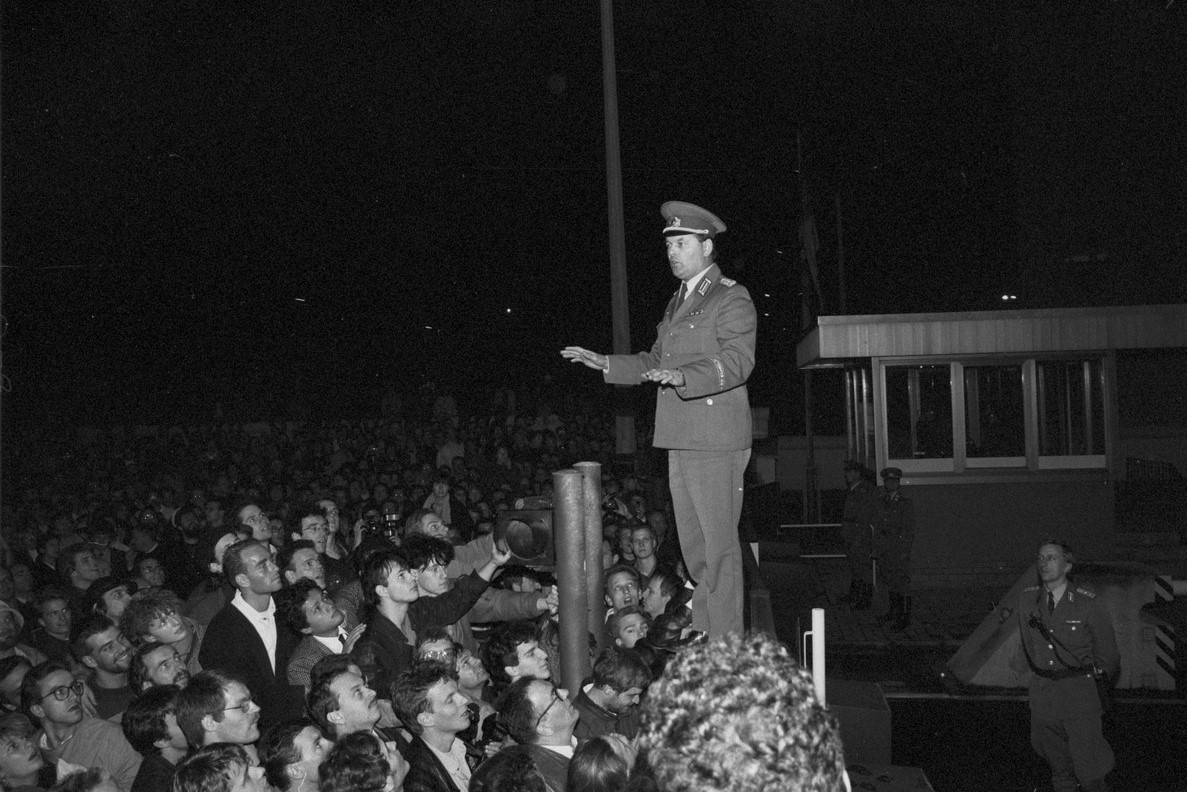 Schrz-weiß Foto eines Grenzsoldaten bei Nacht, stehend auf einem Tor, davor eine Menschenmenge