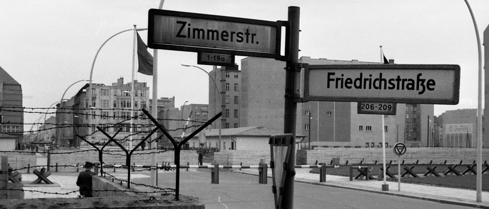 Straßenschild an der Ecke Zimmerstraße und Friedrichstraße, im Hintergrund der Grenzübergang